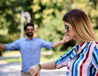 2-3 woman in a striped plaid button up shirt looking at the watch on her wrist as her date is in the background who is late showing poor first date etiquette