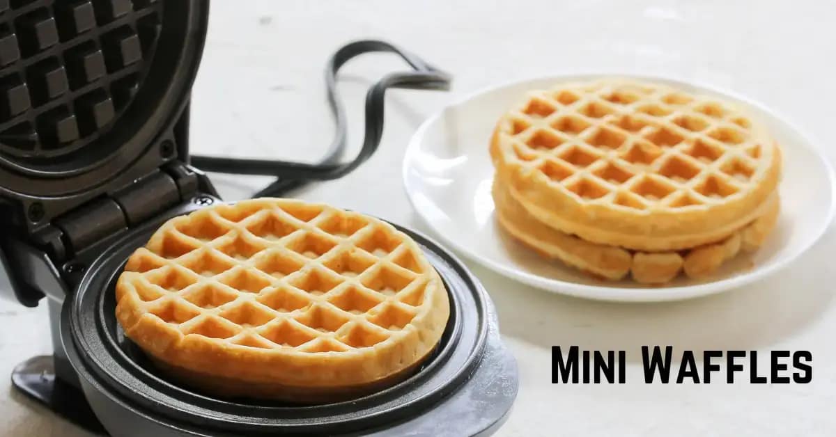 black mini waffle maker placed next to a plate of waffles on a white ceramic plate