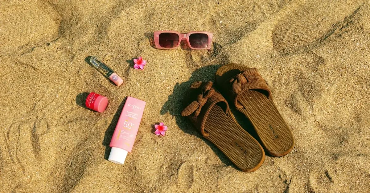 Beach items including flip flops, sunglasses, and a pink purse are laid out on the warm sand, ready for a sunny day.