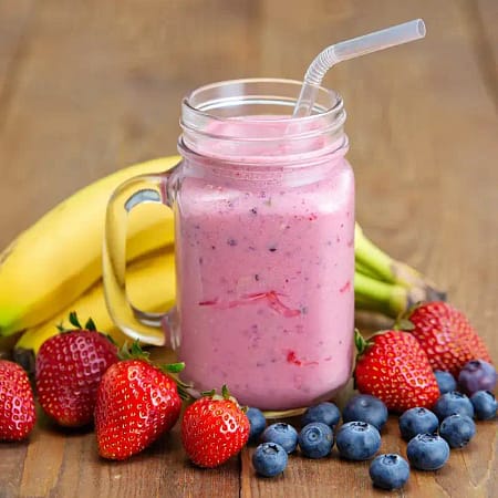 pink smoothie in a glass jar sitting on a table surrounded by a variety of fruits