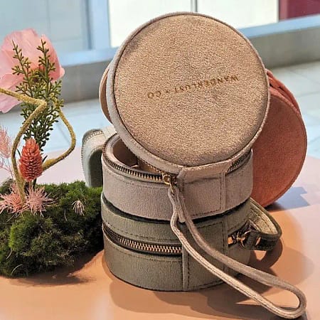 Round suede travel jewelry case with zipper, stacked pastel jewelry organizers as a thoughtful gift idea for women.