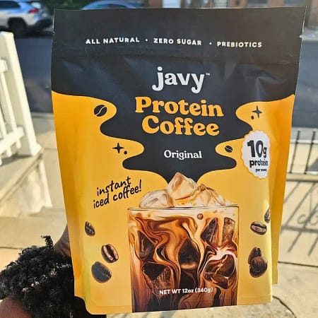 someone holding a bag of protein coffee while standing outside on a bright sunny day