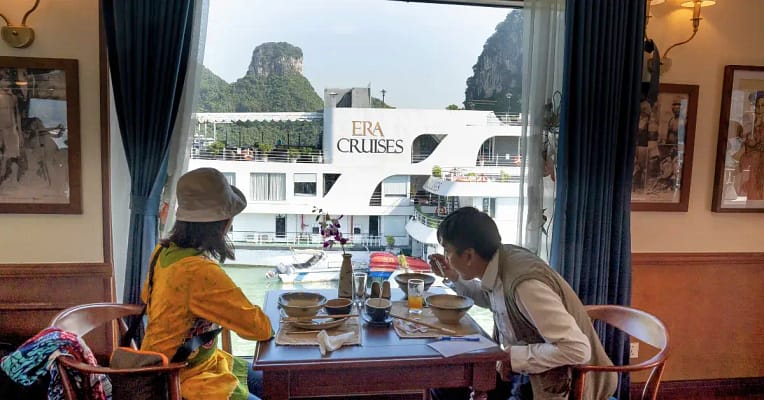 couple a couple sitting down at a table enjoying a beautiful experience as they dine out while looking out the window at a cruise ship.