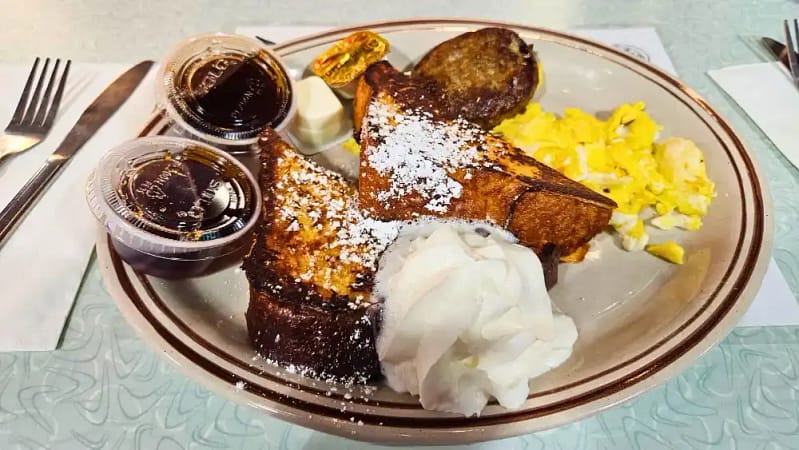 a homestyle breakfast from down home diner featuring golden brown French toast, creamy scrambled eggs and a sausage patty
