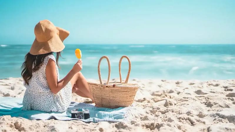 woman sitting on top of a beach towel at a summer beach enjoying a relaxing beach weekend trip