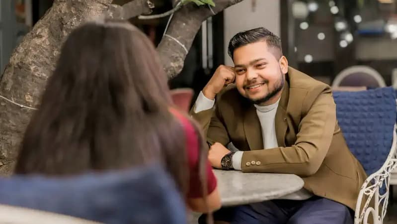 two people on a first date sitting at a table across from one another with the man smiling at the woman