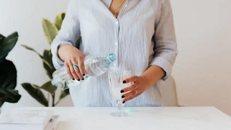 woman in a striped button down shirt wearing black nail polish pouring water in a glass cup