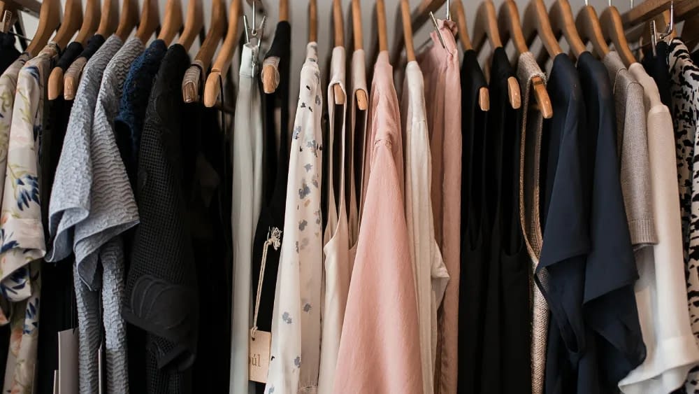a closet full of of dark and bright clothes hanging on wood hangers
