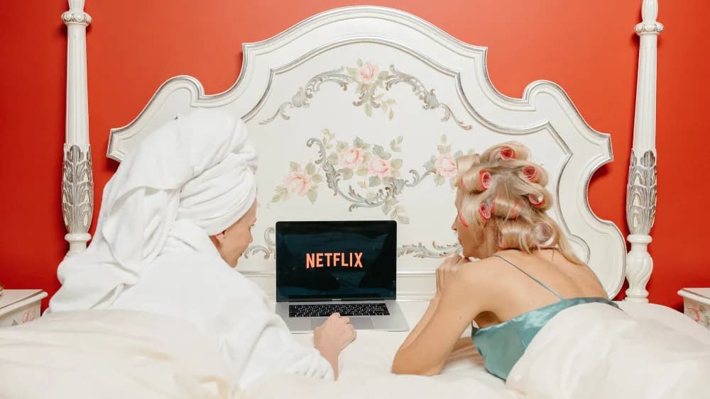 two women laying in bed watching Netflix on a Mac book pro laptop