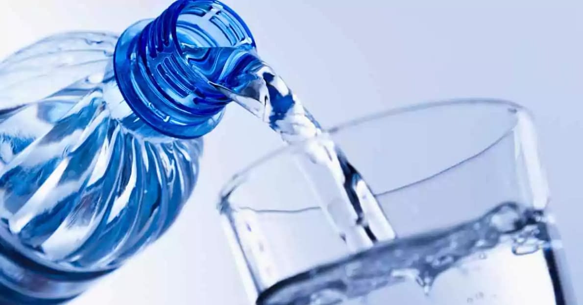 a bottle of water being poured into a clear glass cup one of many tiricks to help hydrate yourself from the inside and out while also promoting health