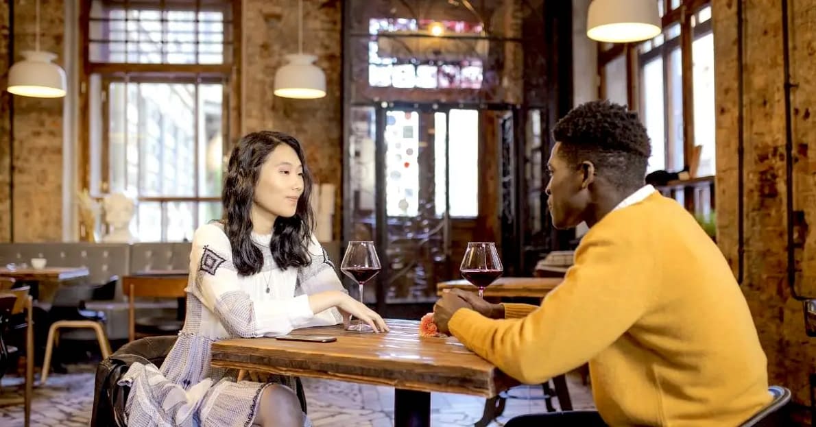 two people sitting at a table inside of a restaurant on a first date with one person oversharing too soon their personal information a no no for first date etiquette
