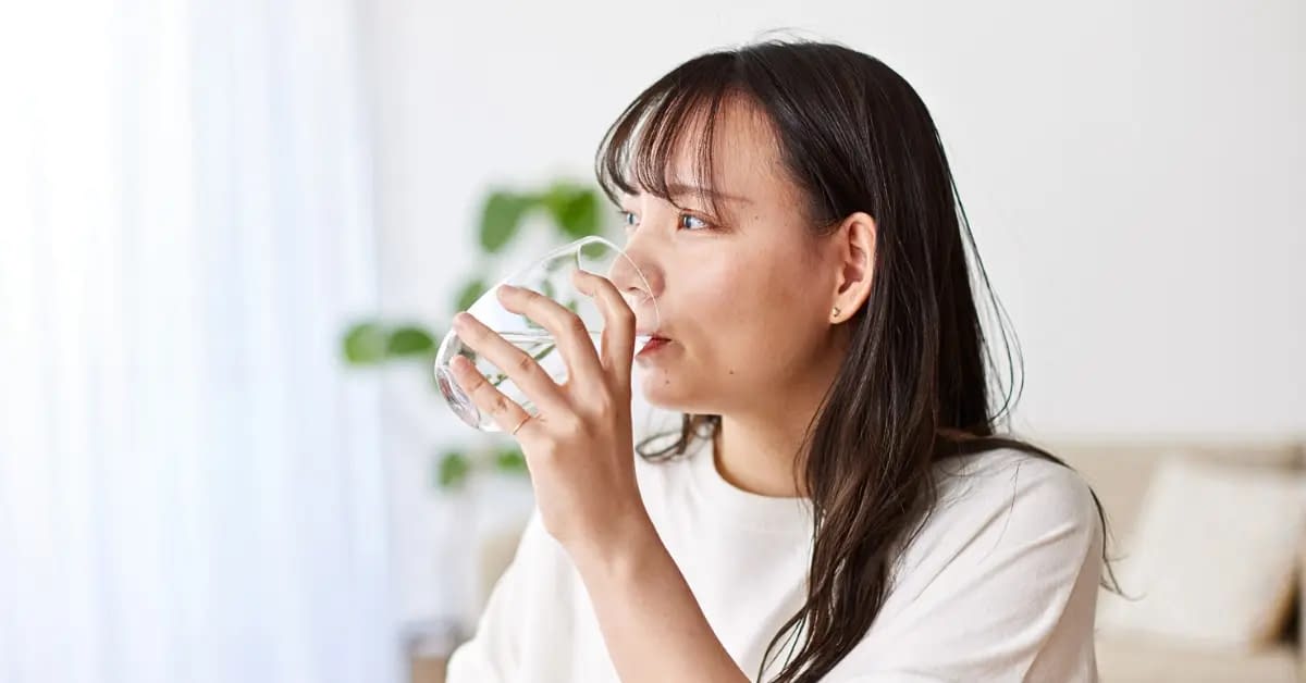 woman with dark hair practicing hydration hacks by drinking a glass of water