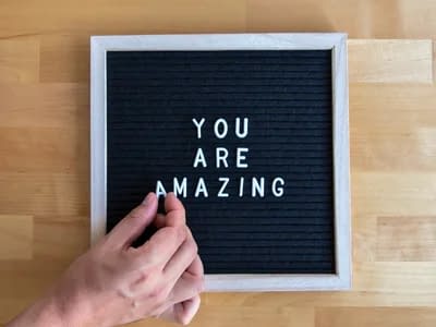 A white and black letter board displaying the phrase "You Are Amazing" in colorful letters against a wooden background.