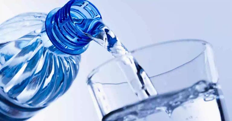 a bottle of water being poured into a clear glass cup one of many tiricks to help hydrate yourself from the inside and out while also promoting health