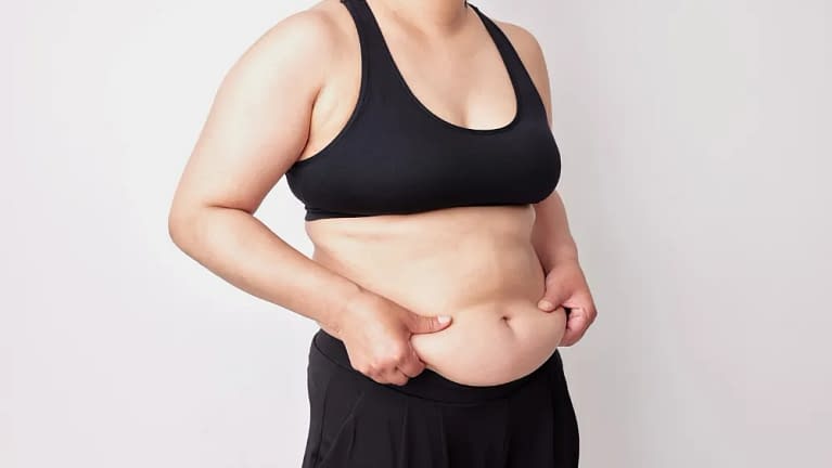 chubby woman wearing a sleeveless black tank top and sweatpants holding her stomach to face her insecurities