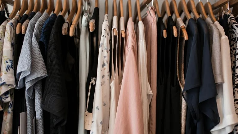 a closet full of of dark and bright clothes hanging on wood hangers