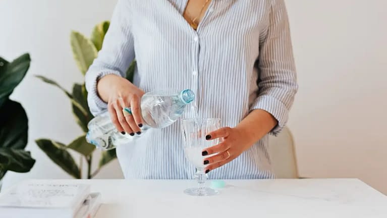 woman in a fitted button down shirt pouring a bottle of water in a tall wine glass