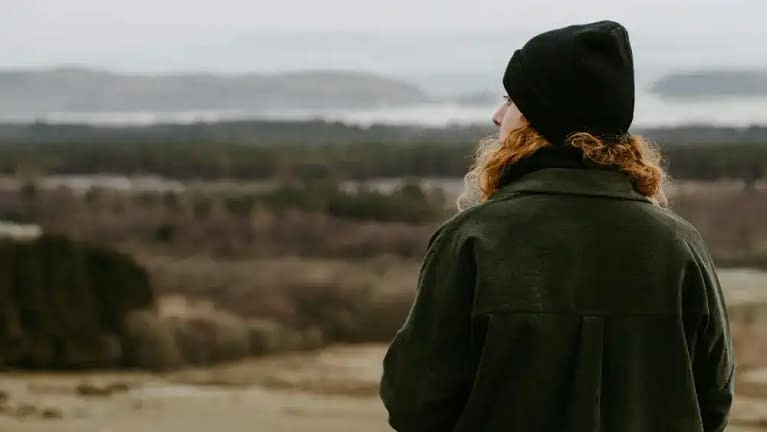 a white man or woman with red curly/wavy hair enjoying a walk on their fall weekend trip wearing a black beanie and dark green olive jacket