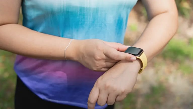 woman exercising outside wearing a Samsung fitness tracker with a yellow band to help keep track of her hydration hacks