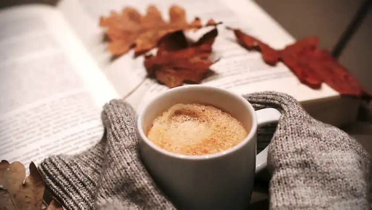 warm and cozy fall weekend scene featuring a ceramic white mug filled with a hot drink along with a good book to read