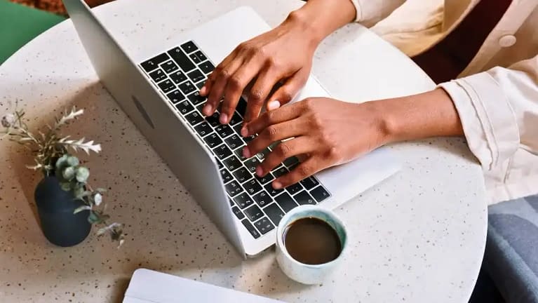 person sitting at desk typing up blog post ideas on their macbook laptop