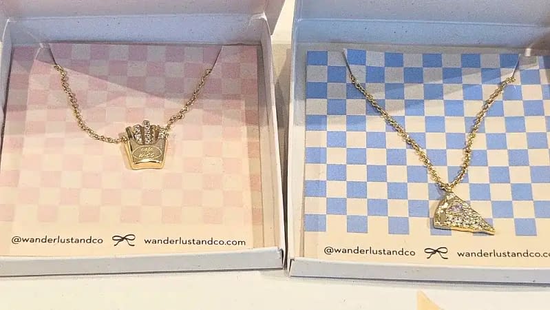 2 gold necklaces each in a wanderlust + co box. on the left is the fries necklace and on the right is the pizza necklace from the grand opening perfect gifts for mom