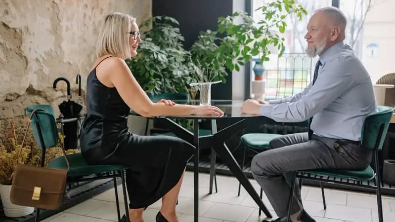 a white woman in a black dress sitting at with a man at a casual restaurant