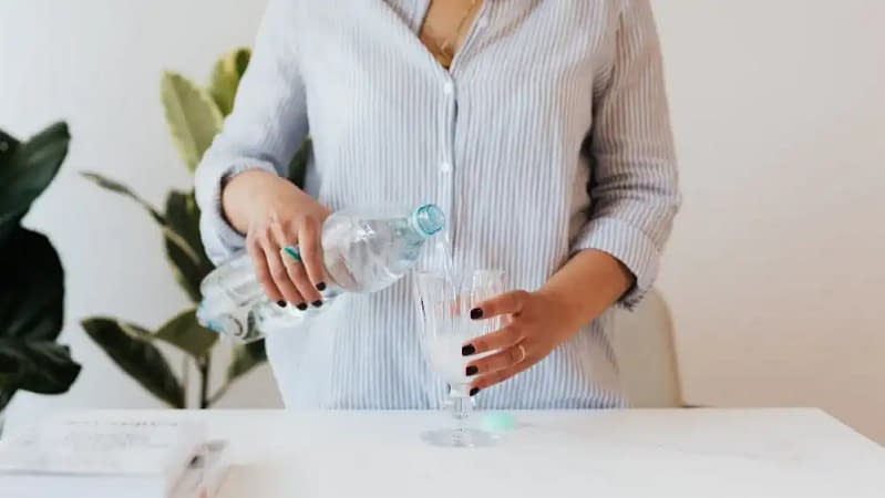 woman in a striped button down shirt wearing black nail polish pouring water in a glass cup